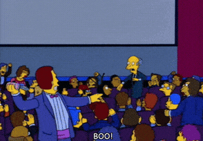 A Man In A Tuxedo Stands In Front Of A Crowd And Says Boo On The Screen GIF
