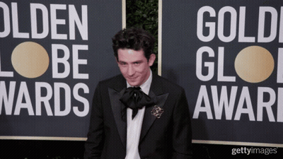 A Man In A Tuxedo Stands In Front Of A Sign That Says Golden Globes GIF