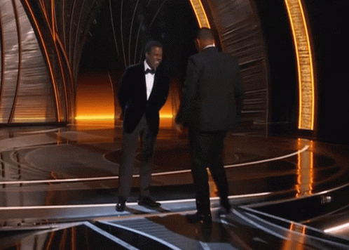 A Man In A Tuxedo Stands Next To Another Man GIF