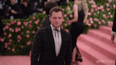 A Man In A Tuxedo Stands On A Red Carpet GIF
