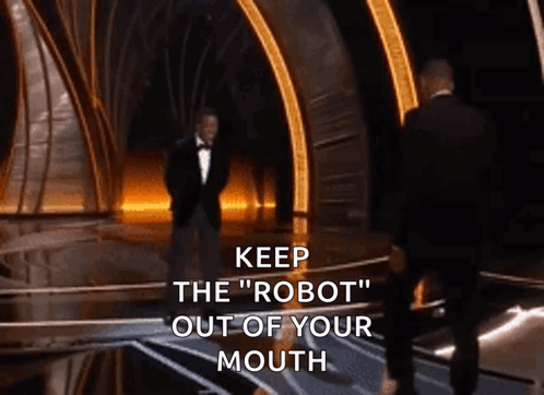 A Man In A Tuxedo Stands On A Stage With The Words " Keep The Robot Out Of Your Mouth " Written Below Him GIF