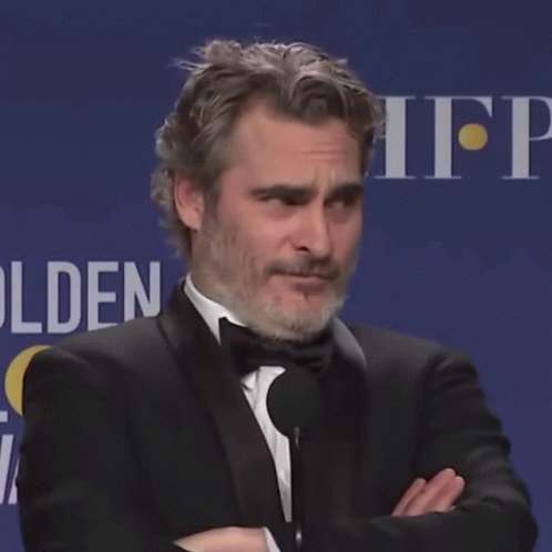 A Man In A Tuxedo Stands With His Arms Crossed In Front Of A Sign That Says Hfp GIF