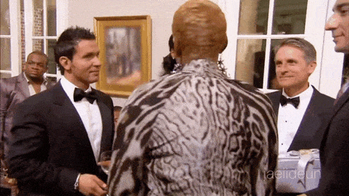 A Man In A Tuxedo Talks To A Woman In A Leopard Print Dress GIF