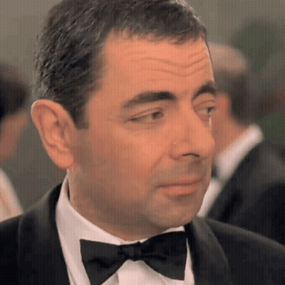 A Man In A Tuxedo With A Bow Tie Looks At The Camera GIF