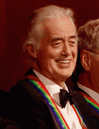 A Man In A Tuxedo With A Rainbow Ribbon Around His Neck Is Smiling GIF