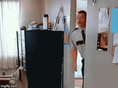A Man In A Uniform And Tie Is Standing In A Doorway Looking Into A Room . GIF