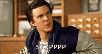 A Man In A Varsity Jacket Is Sitting In A Room And Making A Face . GIF
