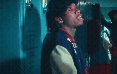 A Man In A Varsity Jacket Is Standing In Front Of Lockers GIF