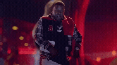 A Man In A Varsity Jacket Is Standing In Front Of The Word Pop It GIF