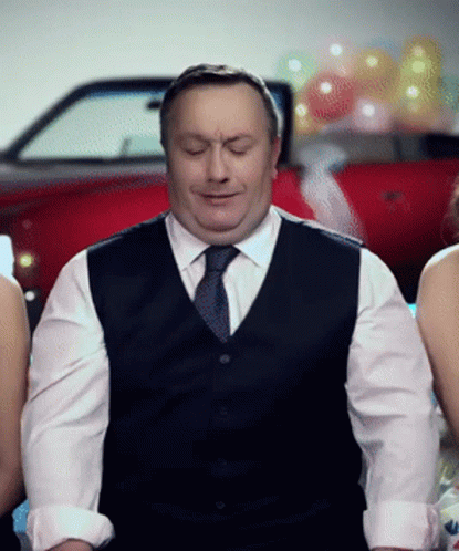 A Man In A Vest And Tie Is Sitting In Front Of Two Women GIF