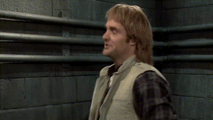 A Man In A Vest And Tie Is Standing In Front Of A Brick Wall With The Word Sho Written On It . GIF