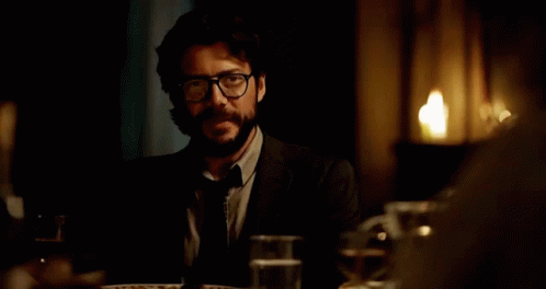 A Man In A Vest And Tie Sitting At A Table GIF
