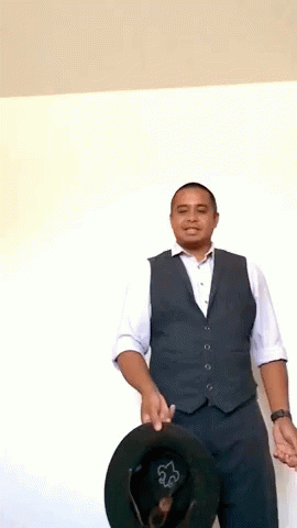 A Man In A Vest And White Shirt Holds A Black Hat GIF