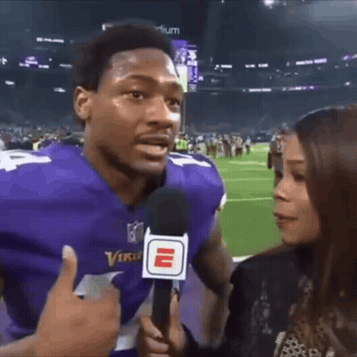 A Man In A Vikings Jersey Is Being Interviewed By A Woman . GIF
