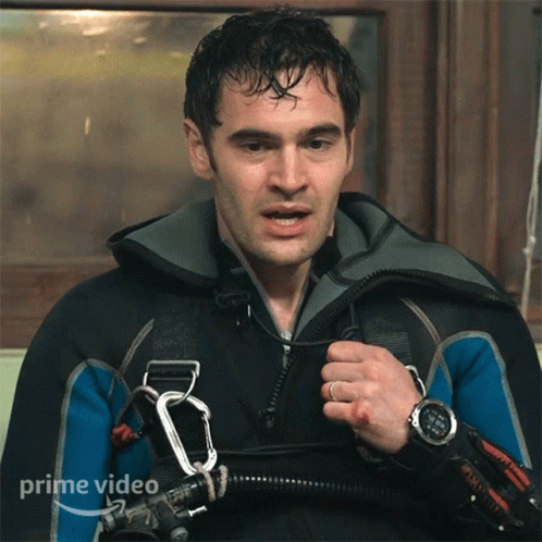 A Man In A Wet Suit Is Holding A Carabiner And A Watch That Says Prime Video On It GIF