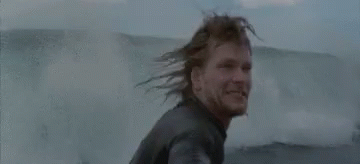 A Man In A Wet Suit Is Standing In The Water And Smiling . GIF