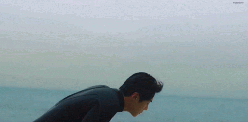 A Man In A Wetsuit Is Bending Over In The Ocean GIF