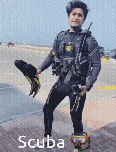 A Man In A Wetsuit Is Holding A Pair Of Scuba Masks GIF