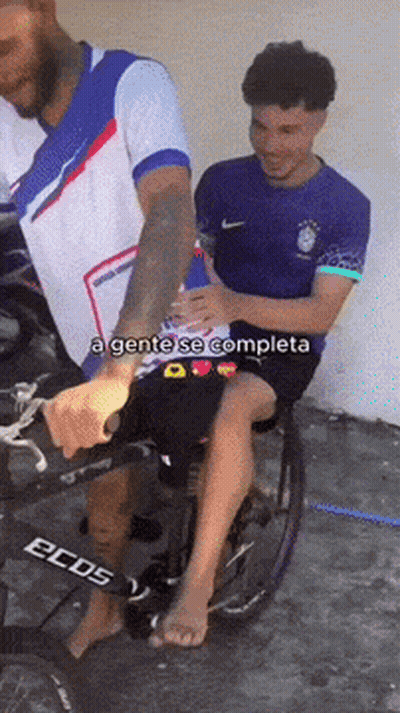 A Man In A Wheelchair Is Being Helped By A Man In A Nike Shirt GIF