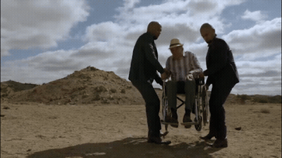 A Man In A Wheelchair Is Being Pushed By Two Men In The Desert GIF
