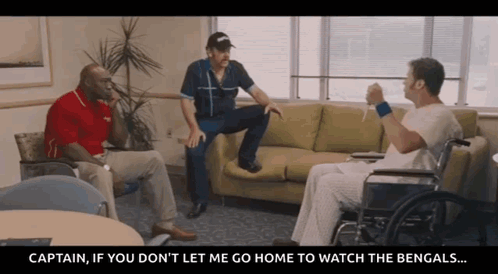 A Man In A Wheelchair Is Sitting On A Couch Talking To Two Other Men GIF