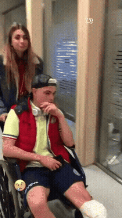 A Man In A Wheelchair With A Bandage On His Leg Is Being Pushed By A Girl GIF