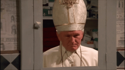 A Man In A White And Gold Hat Is Looking Out Of A Window GIF