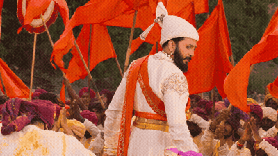 A Man In A White And Orange Costume Stands In Front Of A Crowd Of People Holding Orange Flags GIF