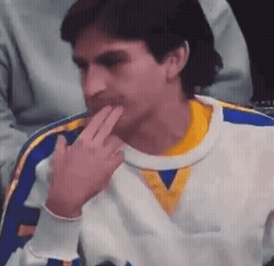 A Man In A White And Yellow Sweater Is Sitting In A Chair With His Hand On His Chin . GIF