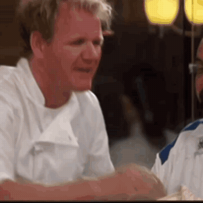 A Man In A White Chef 'S Coat Is Sitting At A Table With A Woman . GIF