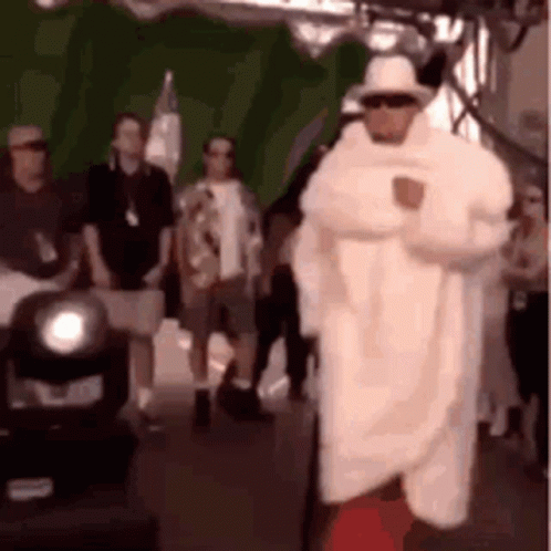 A Man In A White Coat And Hat Is Standing In Front Of A Crowd . GIF