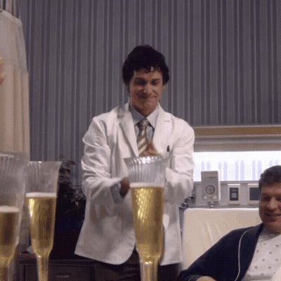 A Man In A White Coat And Tie Is Pouring A Glass Of Beer GIF