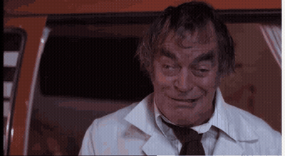 A Man In A White Coat And Tie Is Smiling And Looking At The Camera GIF