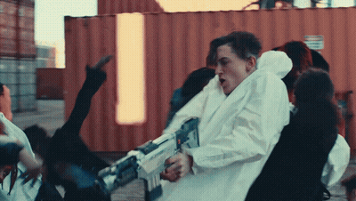 A Man In A White Coat Holds A Gun In A Crowd Of People GIF