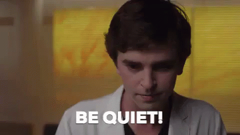 A Man In A White Coat Is Saying `` Be Quiet '' While Standing In Front Of A Window . GIF