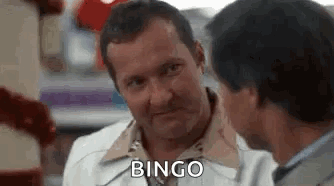 A Man In A White Coat Is Talking To Another Man In A Restaurant And Says `` Bingo '' . GIF