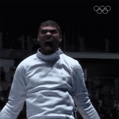 A Man In A White Fencing Uniform Is Screaming With The Olympics Logo In The Background GIF