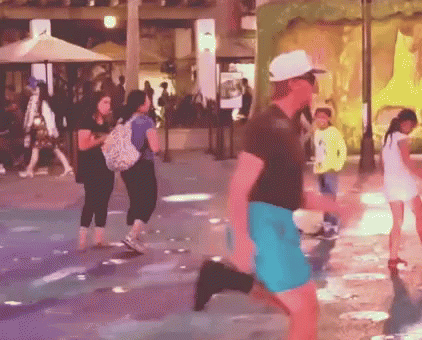 A Man In A White Hat And Blue Shorts Is Running In A Crowded Street GIF