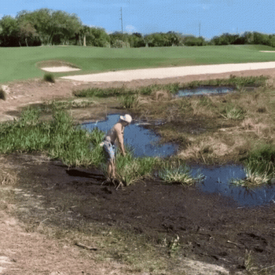 A Man In A White Hat Is Standing In A Puddle Of Water Near A Golf Course GIF
