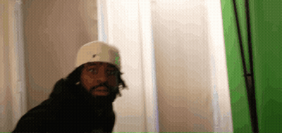 A Man In A White Hat Is Standing In Front Of A Green Screen . GIF