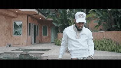 A Man In A White Hat Is Standing In Front Of A Large House . GIF