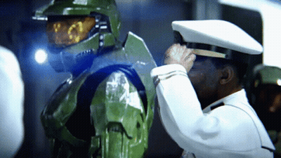 A Man In A White Hat Salutes Another Man In A Green Suit GIF
