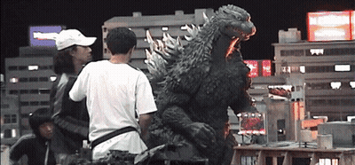 A Man In A White Hat Stands In Front Of A Giant Monster GIF
