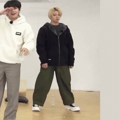 A Man In A White Hoodie And A Man In A Black Jacket Are Standing Next To Each Other On A Wooden Floor . GIF