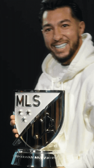 A Man In A White Hoodie Holds A Trophy That Says Mls GIF