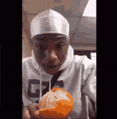 A Man In A White Hoodie Is Holding An Orange In His Hand . GIF