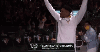 A Man In A White Hoodie Is Raising His Arms In The Air In Front Of A Crowd . GIF