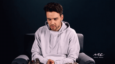 A Man In A White Hoodie Is Sitting In A Chair With A Mc Logo In The Background GIF