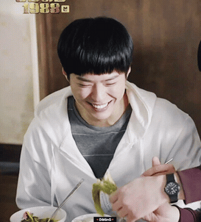 A Man In A White Hoodie Is Smiling While Eating A Meal GIF