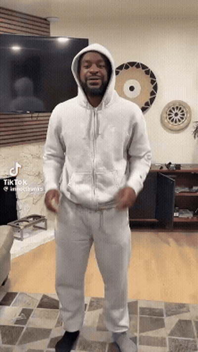 A Man In A White Hoodie Is Standing In A Living Room GIF